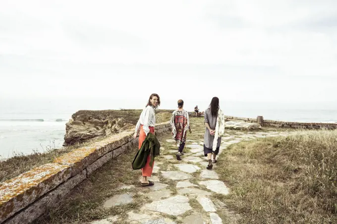 Group of alternative friends walk along coast in summer
