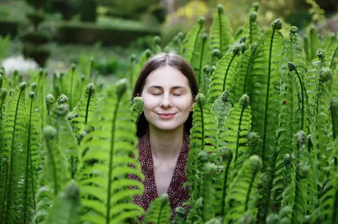 girl enjoys being in nature in middle of young green fern bushes