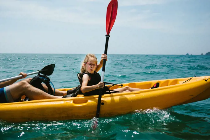 Girl kayaks with her dad on ocean in summer heat