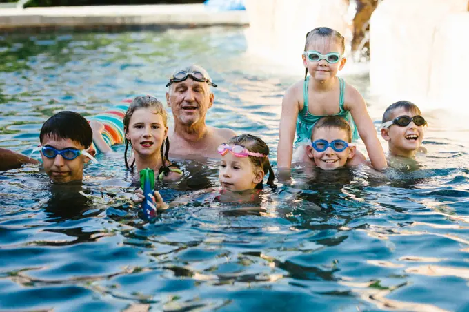 Kids play and splash in swim pool with Grandpa in summer
