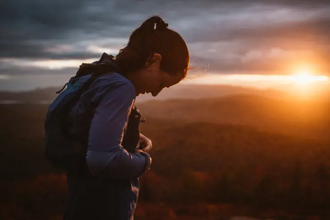 Woman putting on trail running vest at sunset in mountains