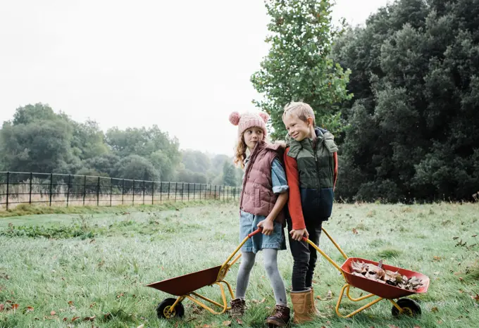 brother and sister holding wheelbarrows foraging outside in autumn