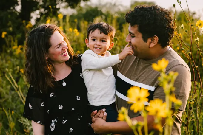 Latino dad and mom laugh with toddler son in flower field