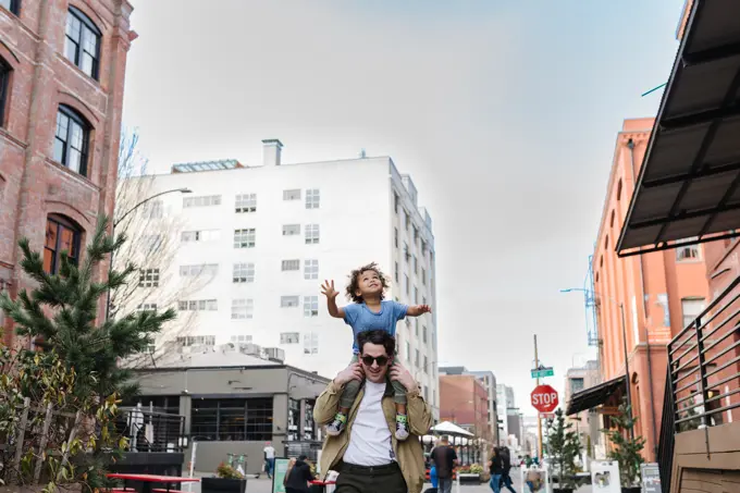 Dad carrying happy biracial toddler on shoulders downtown