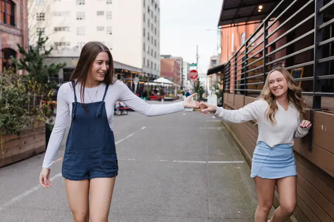 Two women holding hands laughing together downtown