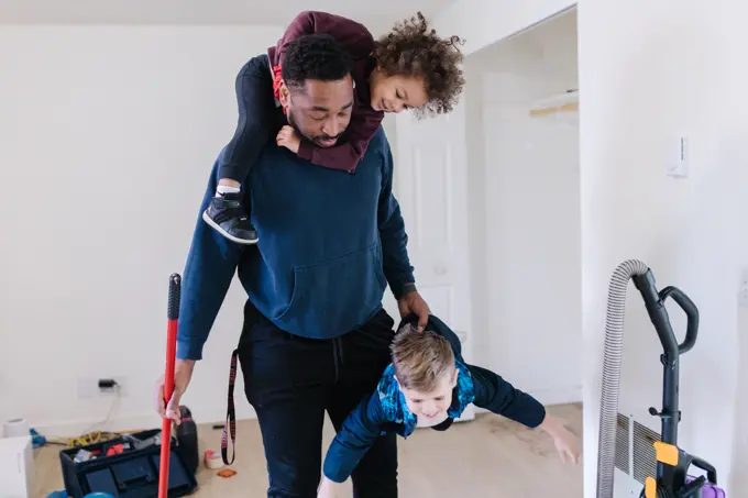 Black dad holding two kids while cleaning the house