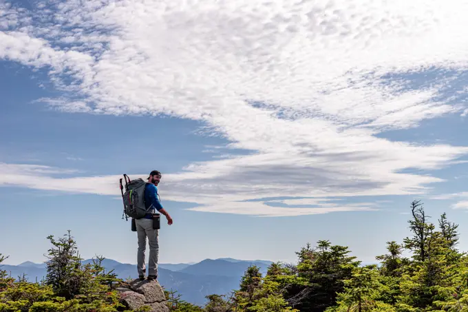 Man in backpack standing on rock at top of mountain.