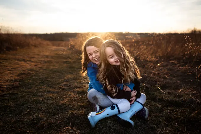 Sisters sitting and smiling in field at sunset