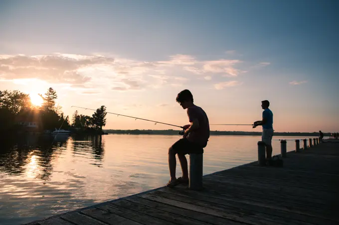 Father and son fishing on a dock of lake at sunset in Ontario, Canada.