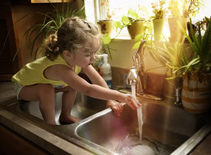 Toddler washing hands with soap in kitchen