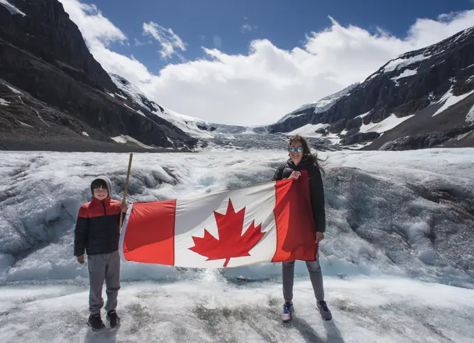 Mother and son holding Canada flag on Athabasca Glacier in Alberta.