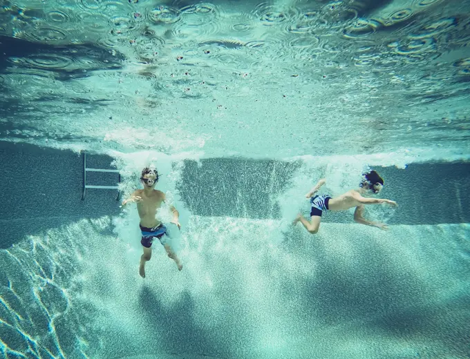 Underwater image of two boys jumping into a swimming pool together.