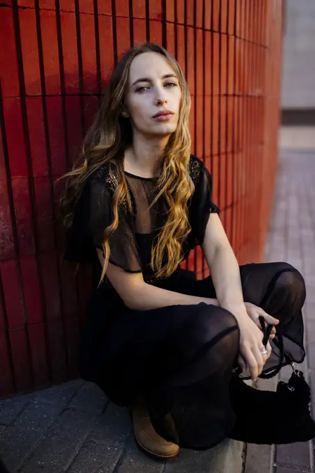 Woman sitting near a red wall in a black dress