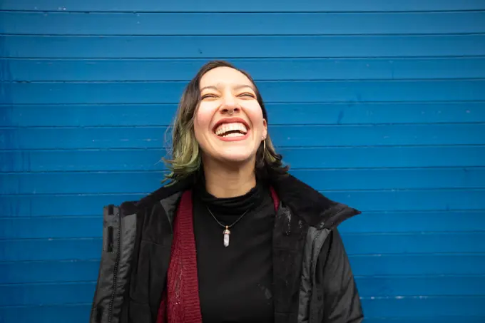 Laughing young woman with closed eyes on blue wall, in rain.