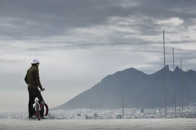 A man with his bike watches a city from a panoramic view point. Monterrey, Mexico.
