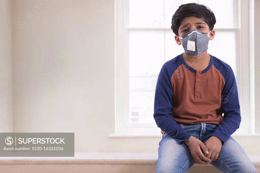 Young boy looking tired of wearing a pollution mask at home. (Children)