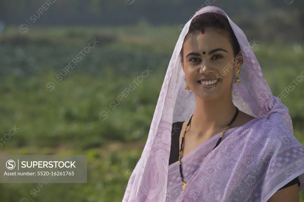 Portrait of a woman standing in an agricultural field with her head covered by saree.