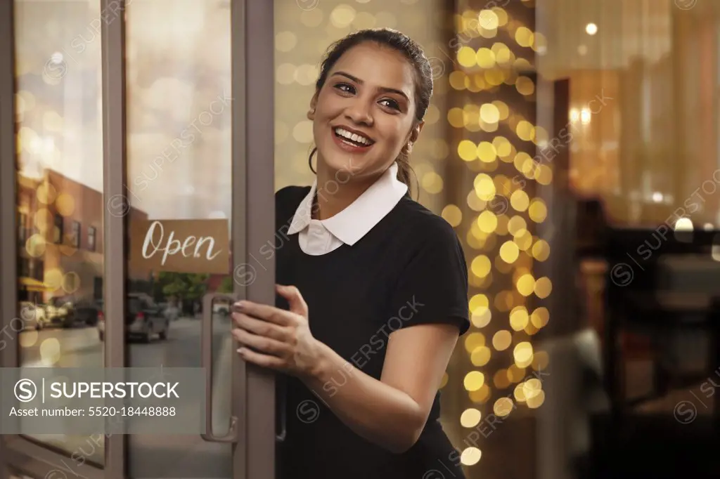 A YOUNG WAITRESS HAPPILY LAUGHING WHILE OPENING DOORS TO RESTAURANT