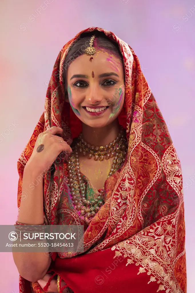 A YOUNG WOMAN IN TRADITIONAL DRESS WITH GULAL ON HER FACE HAPPILY POSING