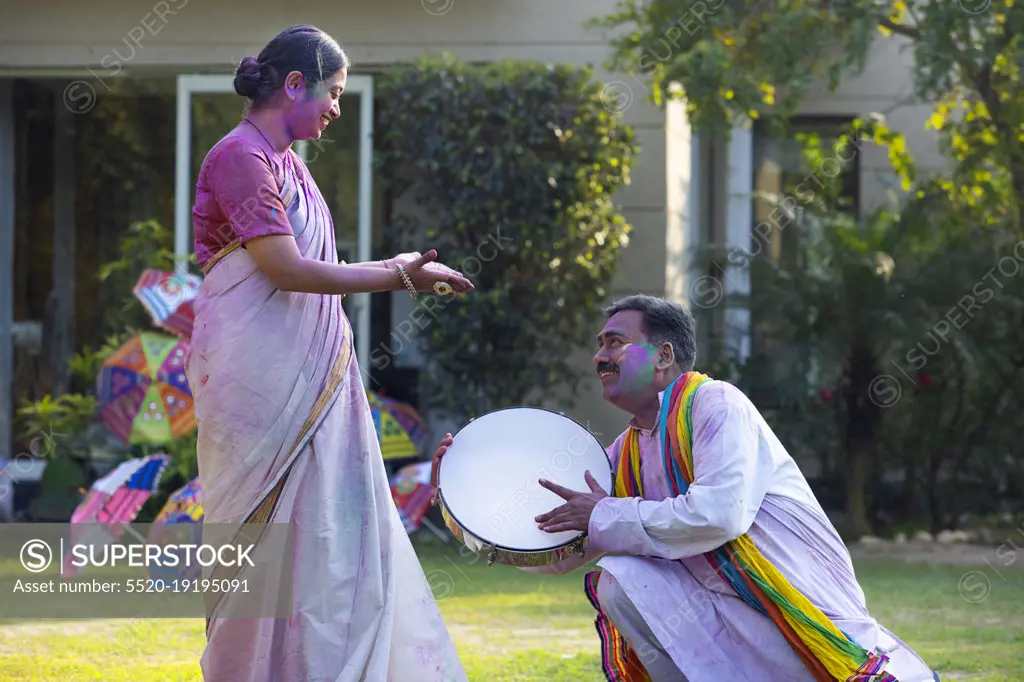 Happy middle aged couple enjoying Holi festival by playing drum