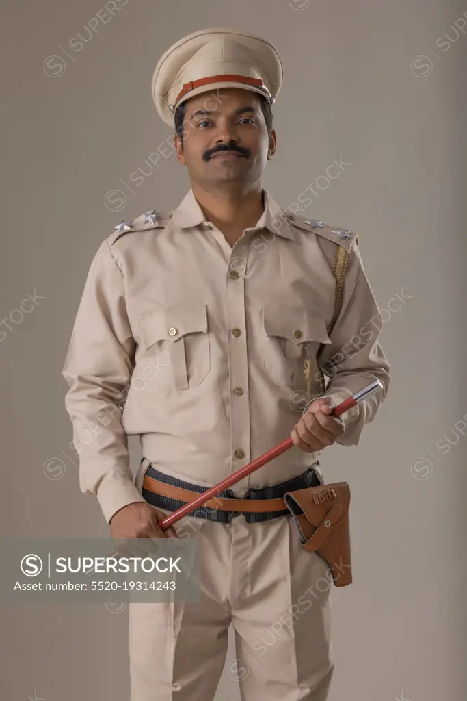 Portrait of an Indian policeman standing with baton in hand