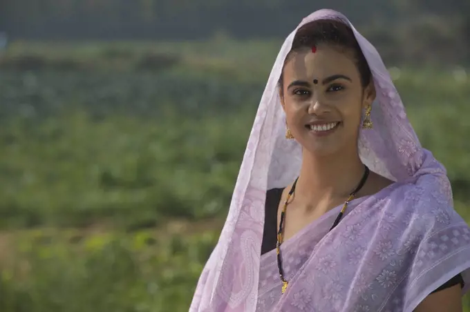 Portrait of a woman standing in an agricultural field with her head covered by saree.
