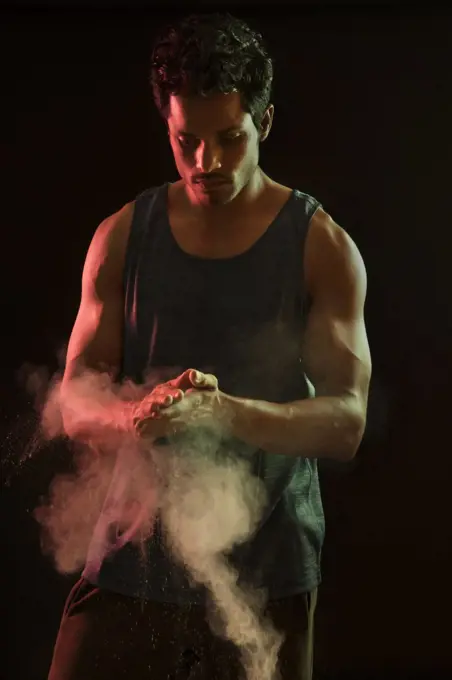 Man standing in front of a dark background with white powder in his hand. 