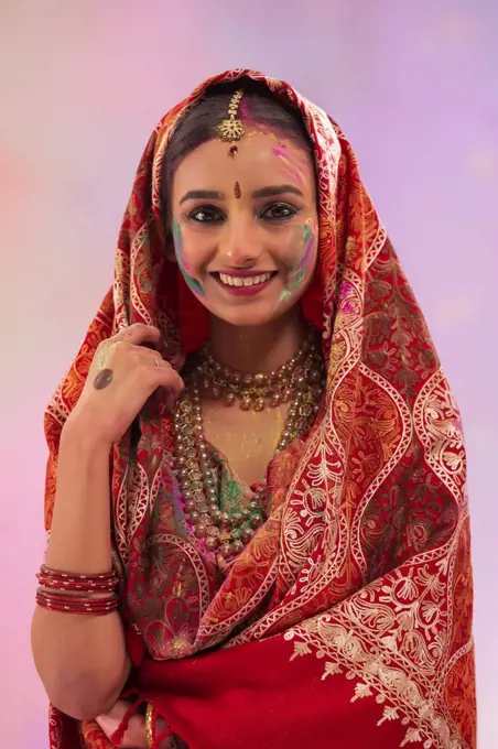 A YOUNG WOMAN IN TRADITIONAL DRESS WITH GULAL ON HER FACE HAPPILY POSING