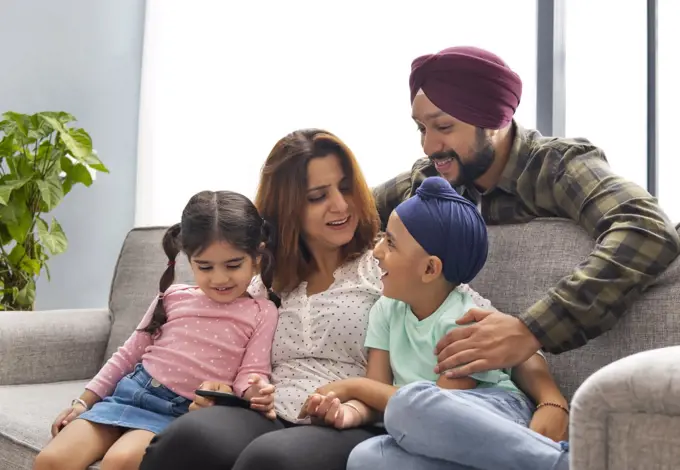 A SIKH FAMILY LAUGHING TOGETHER AND SPENDING TIME TOGETHER SITTING ON SOFA