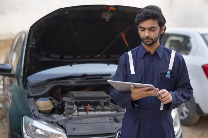 A MECHANIC USING A DIGITAL TABLET TO CHECK THE WORKING OF A CAR