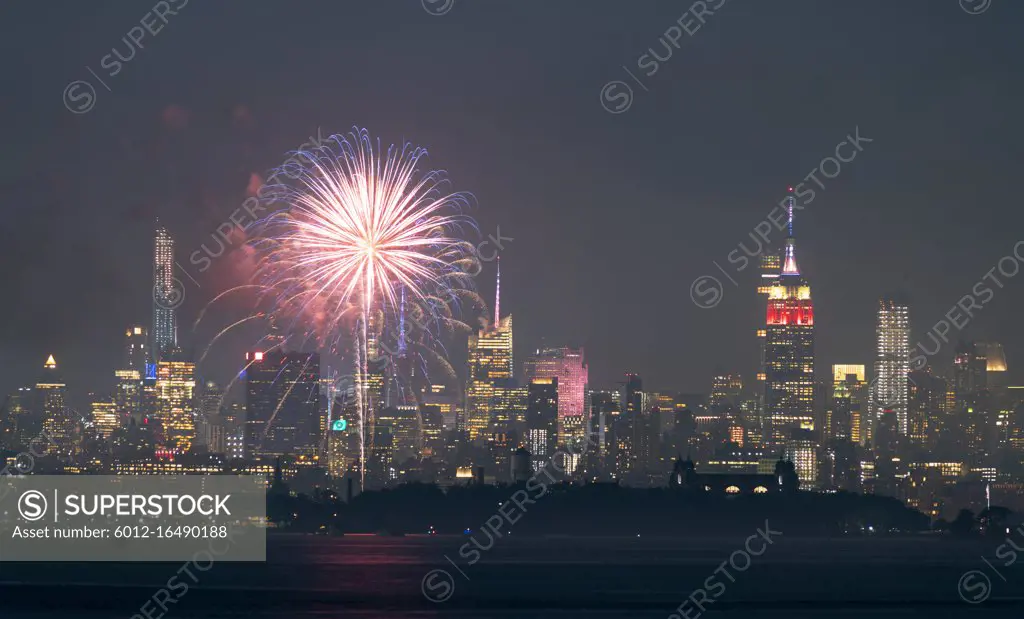 Fireworks are being set off from barges on the river between Jersey City and New York.