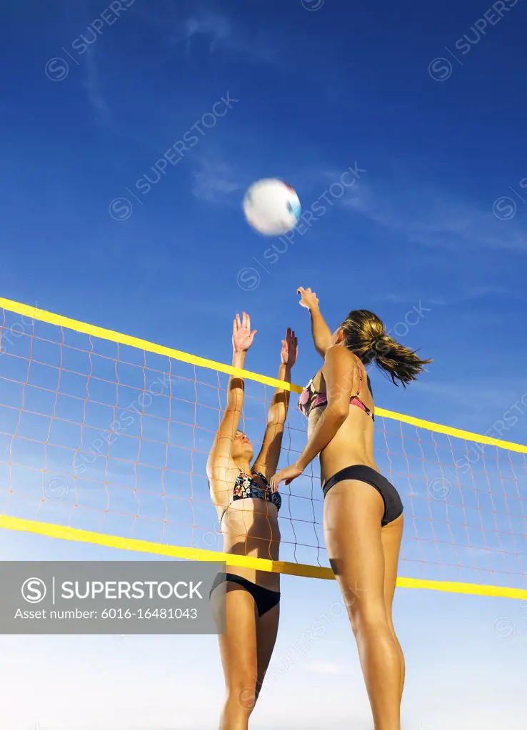 Opposing team members reaching for the volley ball on either side of the net