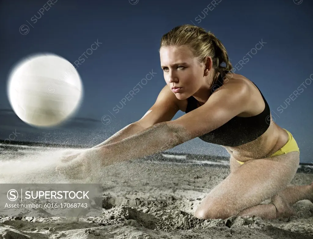 Young woman playing beach volleyball lunging to the sand  to strike the ball upwards