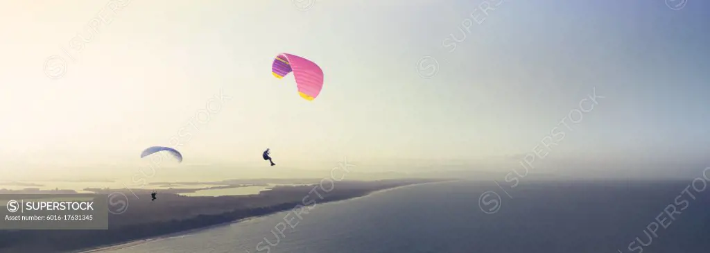 Two people Paragliding over ocean and islands at sunrise