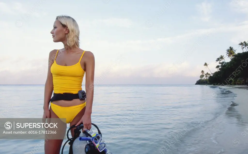 Young woman standing on tropical beach holding her scuba diving gear