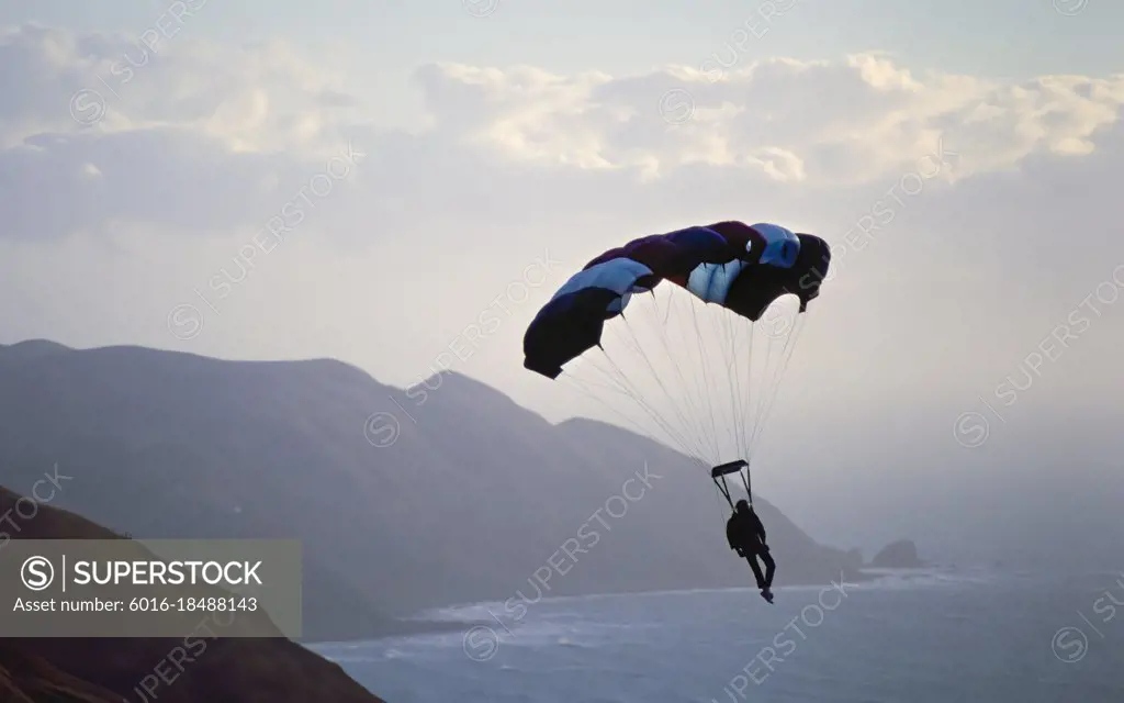 Paragliding off hilly coastline and rough sea below