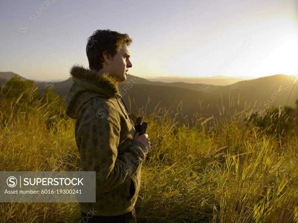 Young man standing in wilderness with binoculars in the golden afternoon light