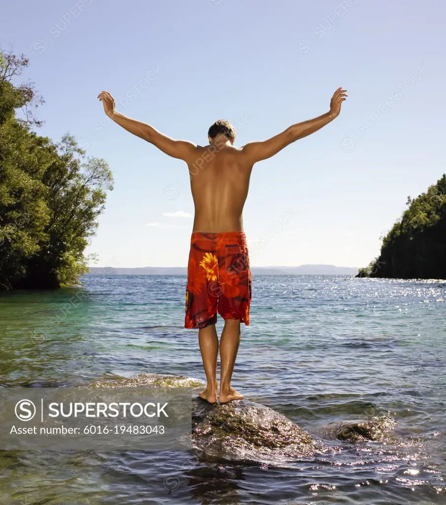 Young man balancing on rock at lake edge