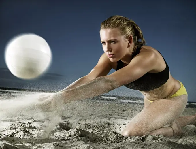 Young woman playing beach volleyball lunging to the sand  to strike the ball upwards