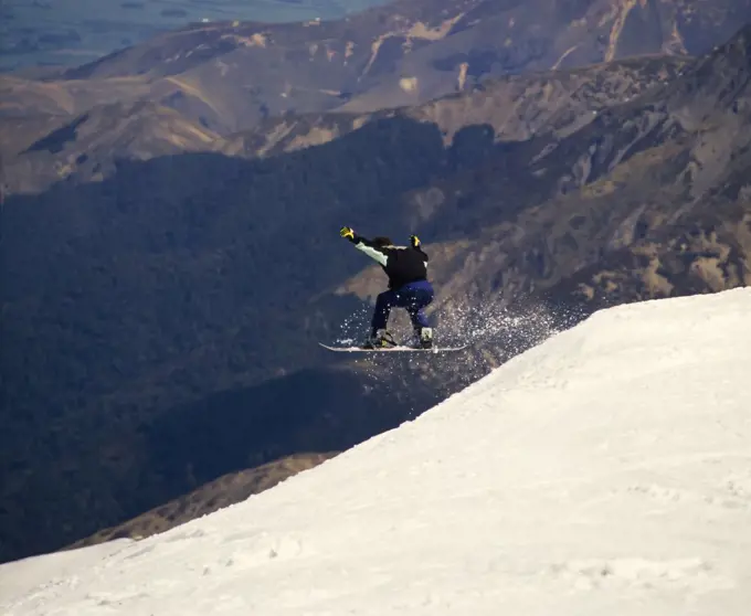 Snowboarder leaping off side of ledge of  snowy Mount Hutt 