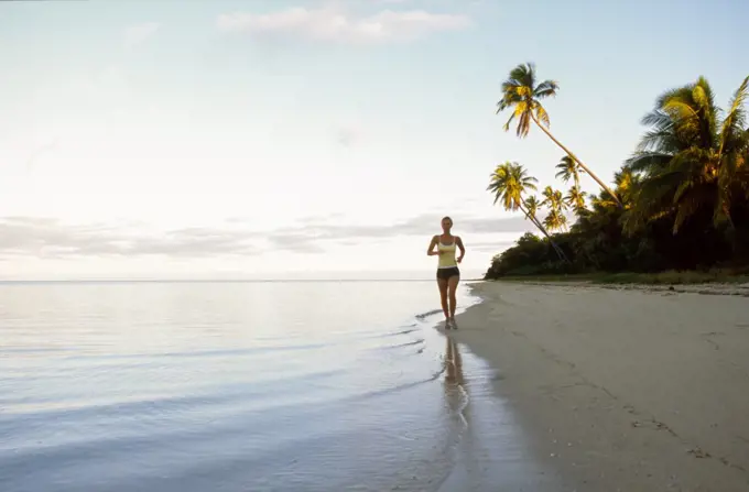Young woman running on tropical beach at sunrise