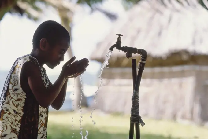 Fijian child drinking water using cupped hands from clean water tap in village