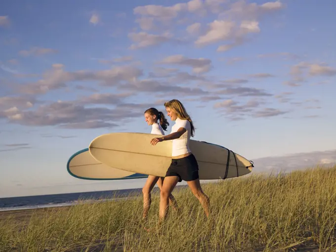 Two young women walking along the beach carrying surfboards