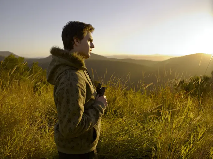 Young man standing in wilderness with binoculars in the golden afternoon light