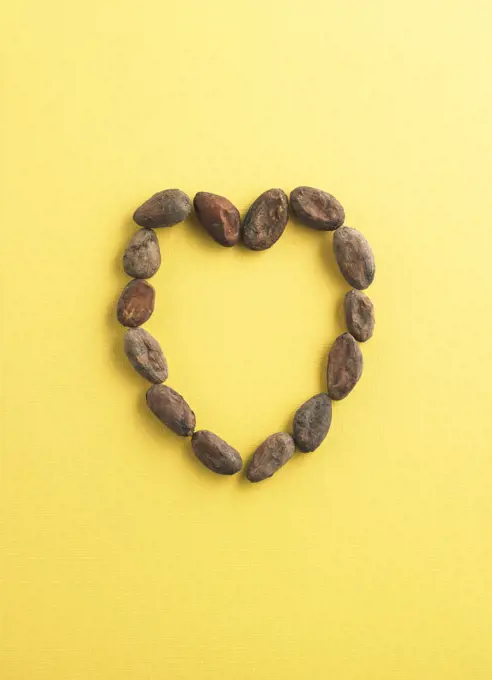 Raw cocoa beans shaped into a heart on yellow background