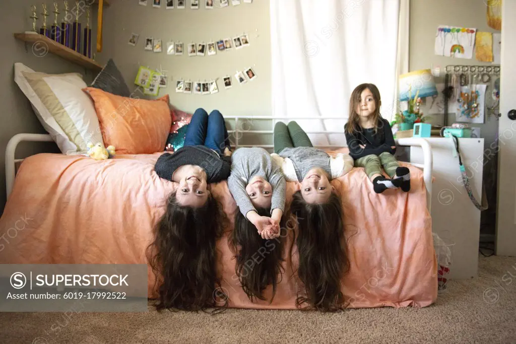 Four happy sisters with long hair laying on a bed together.