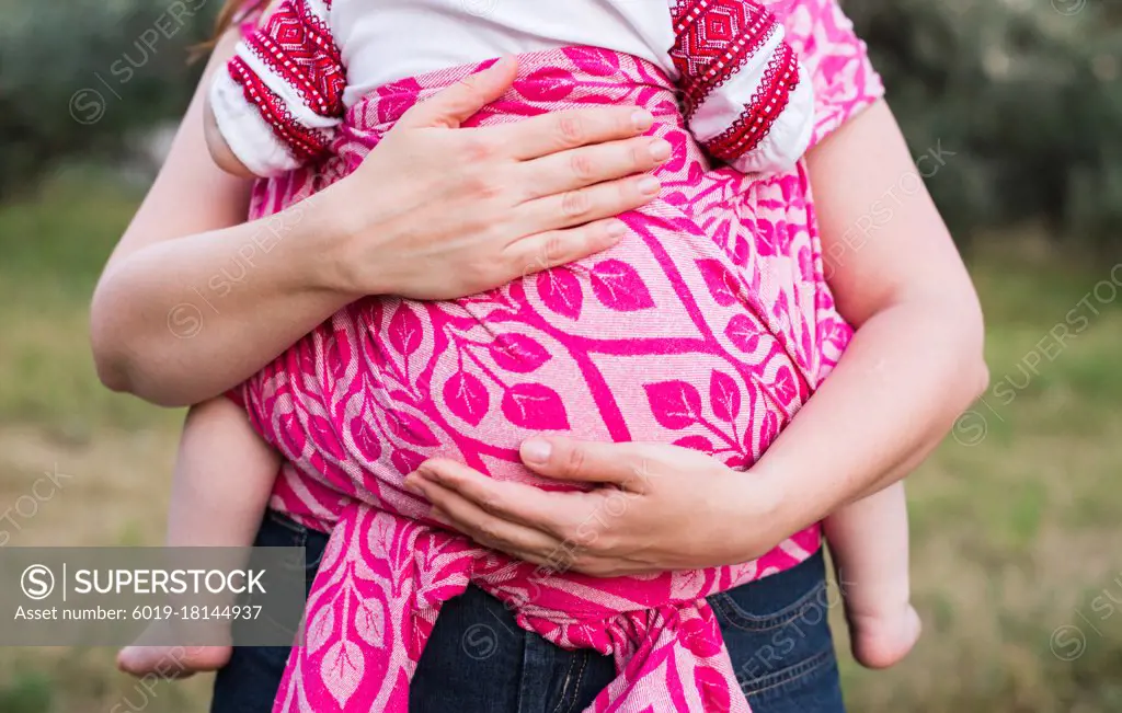 Mother hands hug baby wrapped in pink sling carrier outdoors