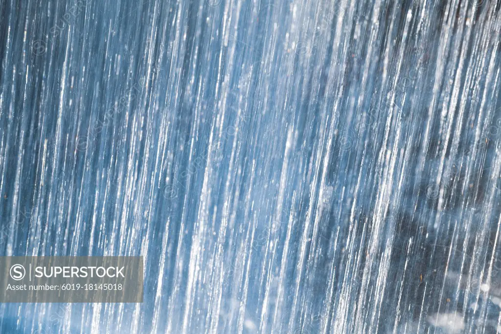 Shot from Behind Waterfall Crashing on Rocks Backlit Abstract