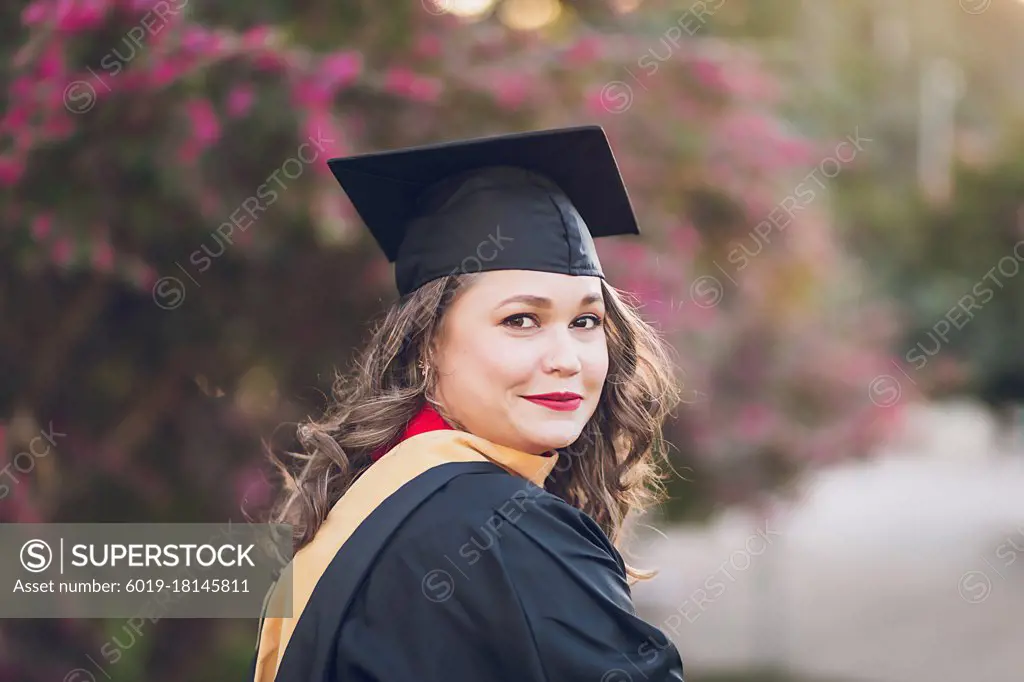 Woman wearing a graduation gown/cap, close to a little smirk.