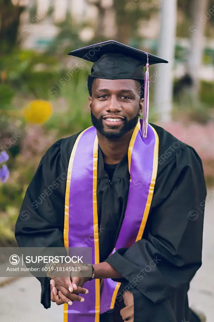 Young man graduating college, wearing a graduation gown/cap.